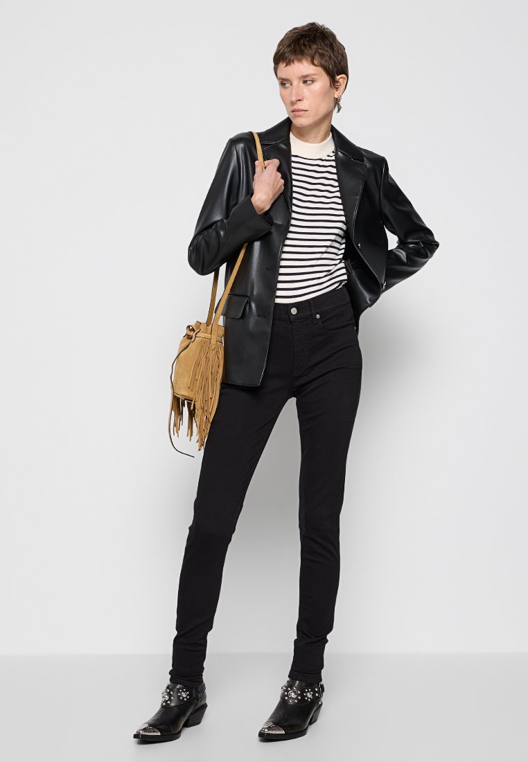 Schwarze Lederblazer über einem gestreiften Hemd, kombiniert mit schwarzen Jeans und verzierten Ankle Boots. Mit einer tanfarbigen Fransen-Tasche accessoriert.