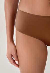 Slip bikini seamless marrone con texture liscia e design a vita bassa, caratterizzato da una vestibilità comoda e dettagli di cucitura minimalisti.