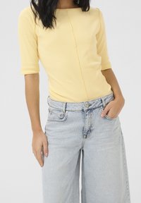 Top giallo a costine con scollo quadrato e maniche a tre quarti, abbinato a jeans larghi blu chiaro. Texture liscia e design casual.