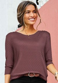 Bordeauxfarbene Bluse mit einem strukturierten Muster aus kleinen weißen Kreisen, mit Rundhalsausschnitt und Dreiviertelärmeln, kombiniert mit einem geflochtenen Gürtel.