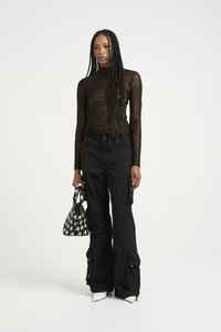 Top lungo in pizzo nero a maniche lunghe, pantaloni cargo neri larghi con tasche con zip, décolleté bianche a punta e una borsa a tracolla nera e bianca con texture.