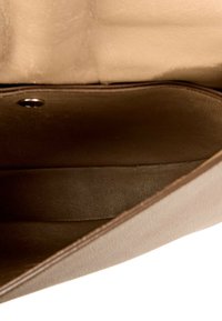 Intérieur vide d'un sac en cuir marron avec un rabat beige ouvert, montrant une doublure lisse et un bouton-pression en métal.