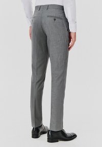 Szare spodnie w prążki o slim fit, z dwiema tylnymi kieszeniami, szlufkami na pasek i gładką teksturą. Noszone z czarnymi butami.