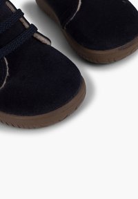 Scarpe scure in suede blu con punta arrotondata, lacci testurizzati e suola in gomma beige, caratterizzate da sottili dettagli di cucitura lungo i bordi.