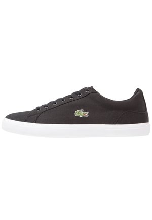 Schwarzer Sneaker mit niedrigem Schaft, weißer Sohle und Schnürdesign, mit kleinem grünem Krokodil-Logo an der Seite.