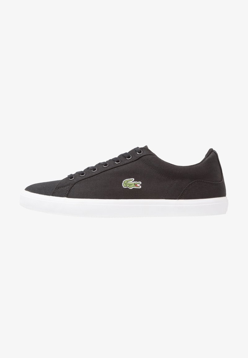 Baskets basses noires avec semelle blanche et lacets, avec un petit logo crocodile vert sur le côté.