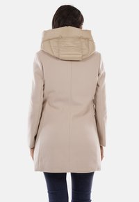 Cappotto beige con finitura testurizzata e cappuccio beige imbottito. Il design è lungo fino al ginocchio, con maniche lunghe e silhouette aderente.