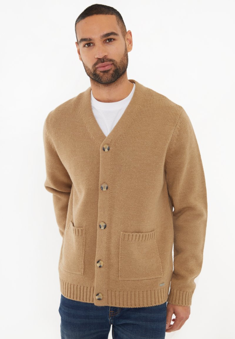 Beige gestrickte Strickjacke mit V-Ausschnitt, sechs Knöpfen, zwei Fronttaschen und gerippten Bündchen und Saum, die eine weiche Textur bietet.