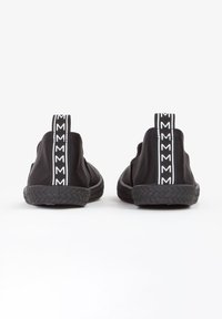 Zwarte instappers met een gestructureerde rubberen zool, stoffen bovenkant en witte logo-geprinte trekstrips aan de achterkant. Gladde, strakke vormgeving.