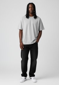 Grijs korte mouwen T-shirt, comfortabele pasvorm, gecombineerd met donkere jeans en witte sneakers met zwarte accenten. Schoon en minimalistisch ontwerp.