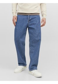 Jeans in denim blu con una vestibilità comoda, dotati di zip e design a cinque tasche. Indossati con una felpa chiara e sneakers bianche.
