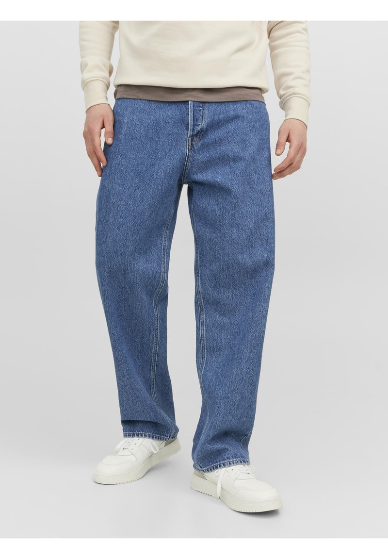 Jeans in denim blu con una vestibilità comoda, dotati di zip e design a cinque tasche. Indossati con una felpa chiara e sneakers bianche.