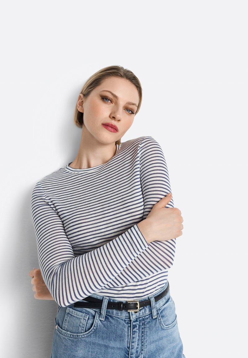 Gestreiftes Langarmoberteil in Marineblau und Weiß, aus leichtem Material. Kombiniert mit hochgeschnittenen hellen Jeans und einem schwarzen Gürtel.