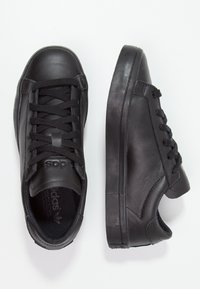 Black leather sneakers with a textured finish, flat rubber sole, rounded toe, and six eyelets for laces. Simple, streamlined design.