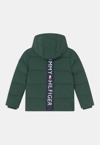 Giacca imbottita verde con cappuccio, caratterizzata da una banda verticale blu navy con il testo "TOMMY HILFIGER". Tessuto liscio, design trapuntato e maniche lunghe.