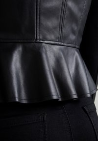 Top peplum in pelle nera con finitura testurizzata, caratterizzato da dettagli sulle cuciture e un orlo arricciato. Vista ravvicinata del materiale e degli elementi di design.
