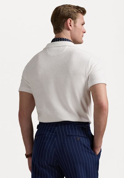 Pull blanc à manches courtes en tricot texturé. Superposé à une chemise marine à pois blancs, associé à un pantalon marine à rayures fines.