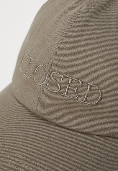 Ruskea baseball-lippis, jossa on brodeerattu "CLOSED"-logo. Kankaassa on hienot, teksturoituneet raidat, ja lippahattu on muotoiltu ja pyöreä.