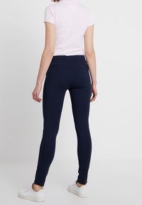 Marineblå leggings med en glat tekstur, slim fit og syning detaljer, parret med en rosa kortærmet polo og hvide sneakers.