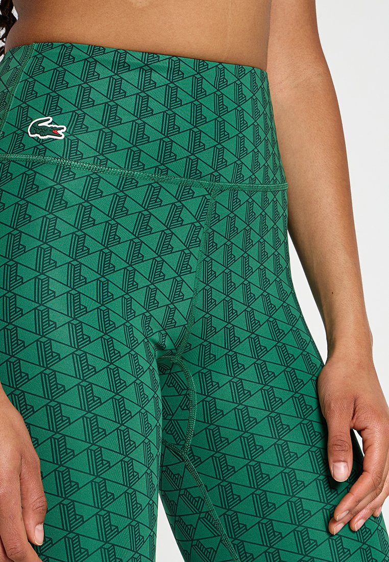 Leggings verdi con un motivo geometrico in nero, vita alta e dettaglio del logo ricamato. Realizzati in materiale elastico e liscio.