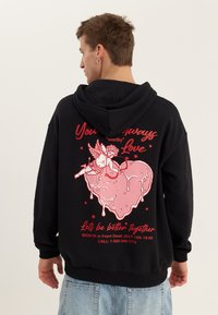 Man wearing black hoodie with pink melting heart and cupid illustration, red text promoting July 14 event and contact information.