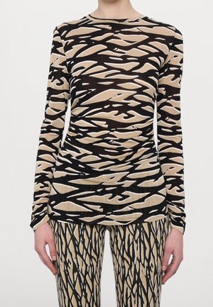 Persoon die een nauwsluitende top met lange mouwen draagt met beige en zwarte abstracte zebrapatronen en bijpassende broek met verticale zwarte en beige patronen.
