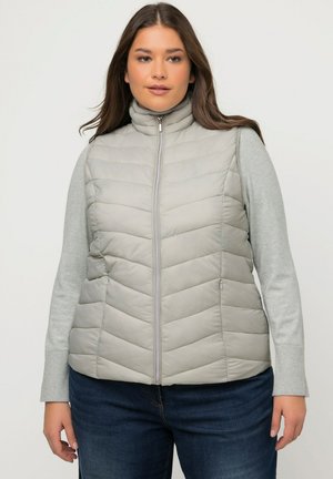 Chaleco acolchado gris claro con un alto cuello, diseño de rombos, cierre de cremallera y bolsillos laterales, superpuesto a una camiseta de manga larga gris claro.
