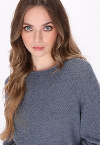 Hellblauer gestrickter Pullover mit strukturiertem Muster, rundem Ausschnitt und langen Ärmeln, vor einem neutralen Hintergrund.