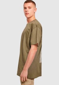 Khaki kortærmet t-shirt lavet af bomuld, med en afslappet pasform, rund hals og et grafisk trykdetalje på ryggen.