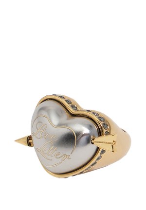 Anillo en forma de corazón de oro y plata con la inscripción "Carta de amor", atravesado por una flecha y adornado con pequeños cristales incrustados.