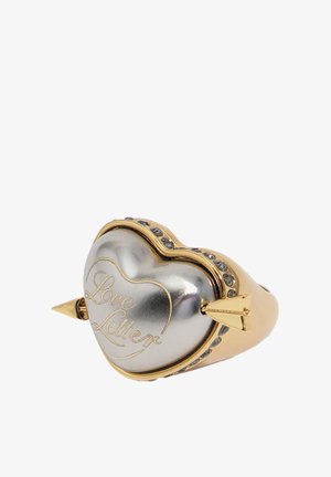 Anillo en forma de corazón de oro y plata con la inscripción "Carta de amor", atravesado por una flecha y adornado con pequeños cristales incrustados.