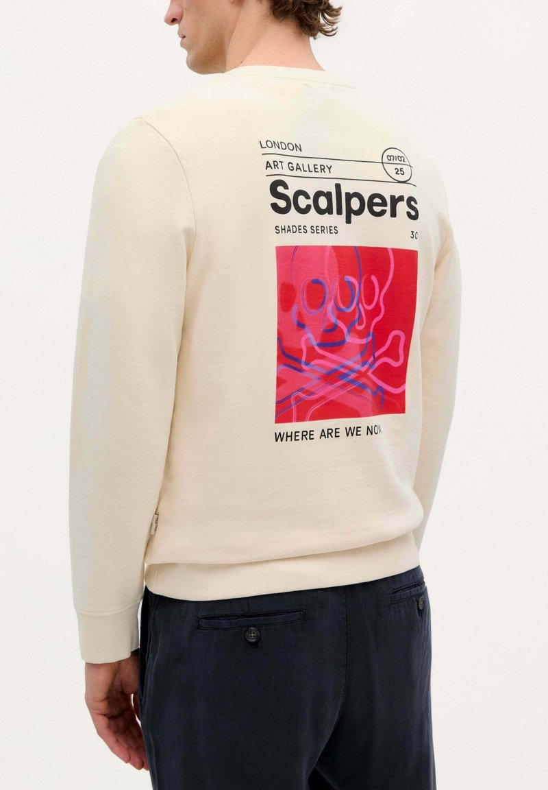 Beige sweatshirt met lange mouwen, voorzien van een rode grafische print van een schedel en gekruiste botten, met zwarte tekst en een relaxte pasvorm.
