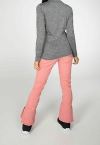 Maglia grigia a maniche lunghe con colletto alto, abbinata a pantaloni rosa svasati con cerniere alle caviglie e sneaker nere.