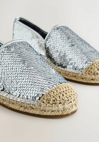 Espadrilles argentées à enfiler, recouvertes de sequins, avec des bouts en jute beige tressé et des semelles intermédiaires sur un fond pâle.