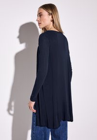 Camiseta de manga larga de color navy con un corte holgado, que cae desde los hombros, con un escote redondo y aberturas laterales. Combinada con jeans de color azul claro.