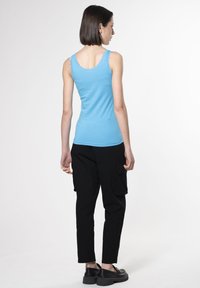 Top in cotone azzurro chiaro con pizzo, abbinato a pantaloni cargo neri. Il modello è mostrato di spalle, evidenziando il design aderente del top.