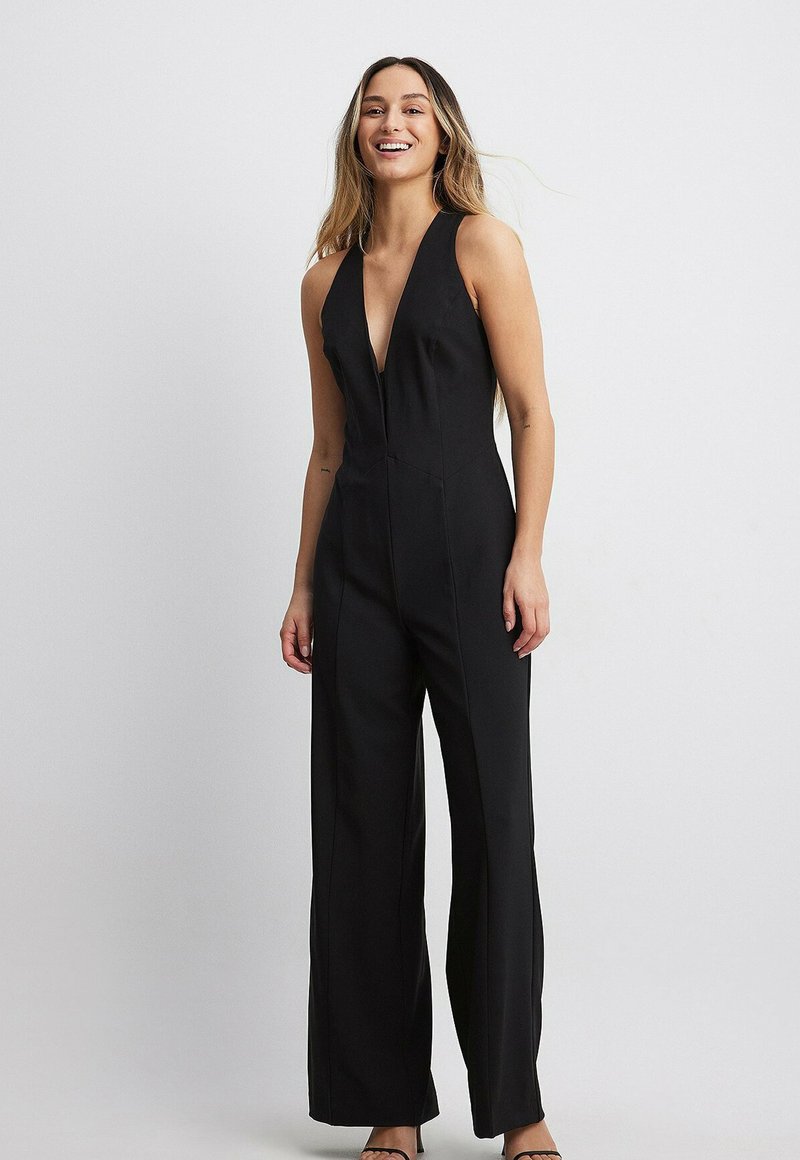 Svart jumpsuit med en djup V-ringning, skräddarsydd passform, vida ben och en mjuk tygfinish. Har minimal sömnad och ingen synlig hårdvara.