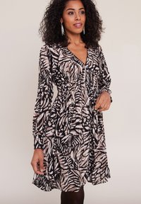 Robe à manches longues avec un imprimé zèbre noir et beige, un décolleté en V, une taille froncée et une jupe fluide arrivant près des genoux.