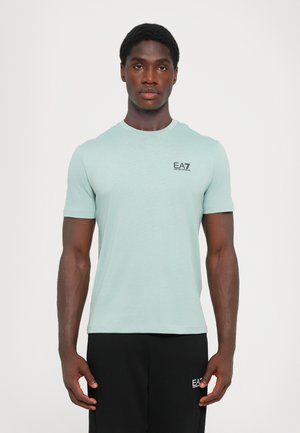 T-shirt vert clair à manches courtes avec un col rond et un petit logo noir EA7 sur la poitrine ; semble fait d'un tissu doux et TEXTURÉ.