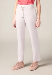 Pantalons de jogging rose clair en tissu doux et lisse avec une taille à cordon et des broderies sur les côtés. Associés à des baskets rose clair.