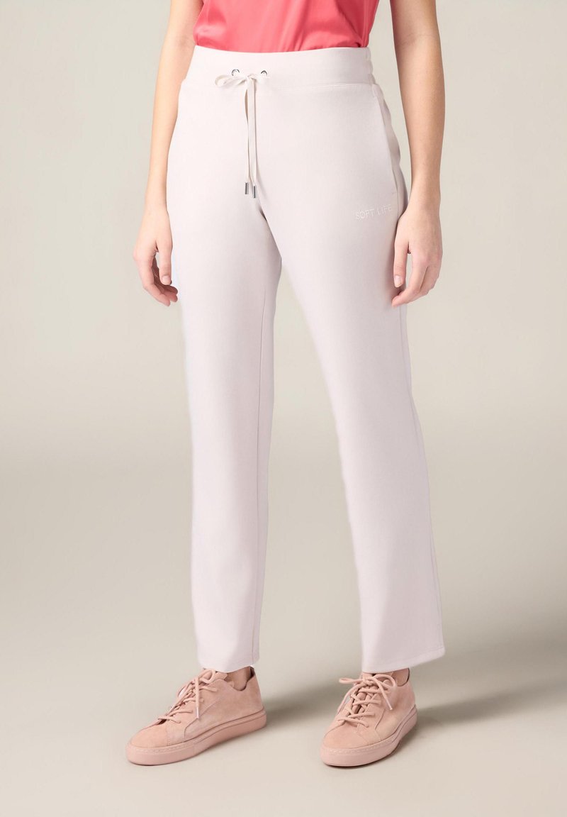 Pantalons de jogging rose clair en tissu doux et lisse avec une taille à cordon et des broderies sur les côtés. Associés à des baskets rose clair.