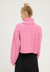 Pull en tricot rose avec un col montant et un ourlet côtelé. La texture est douce et épaisse, avec un design court. Vue de dos présentée.