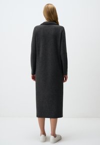 Langes, dunkelgraues Wollkleid mit Kragen, langen Ärmeln und geradem Schnitt, kombiniert mit weißen Sneakers. Glatte Textur.