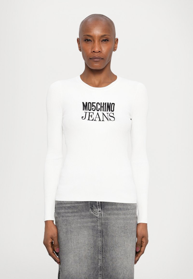 Bela rebrasta dolga majica z dolgimi rukavi, ki vsebuje črn napis "Moschino Jeans". Skupaj zivo v kombinaciji s sivo denimsko krilom za popoln izgled.