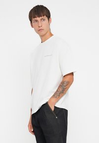 Witte katoenen t-shirt met korte mouwen, ronde hals en een tekstontwerp aan de voorkant. Draagt met donkere spijkerbroeken met een zichtbare naaddetail.