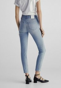 Lichtblauwe skinny jeans met een hoge taille, voorzien van achterzakken en een lichte textuur. Gecombineerd met zwarte enkelsandalen met enkelband.