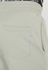 Pantalons de survêtement vert clair en tissu texturé, dotés d'une poche arrière et d'une petite étiquette sur le côté. Ceinture élastique en haut.
