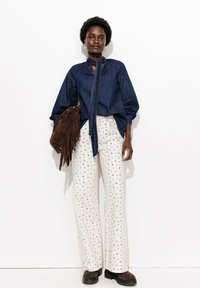 Chemise en denim avec un décolleté en forme de clé, manches bouffantes longues ; pantalon blanc cassé à petit motif floral bleu ; sac à franges marron ; bottes marron.