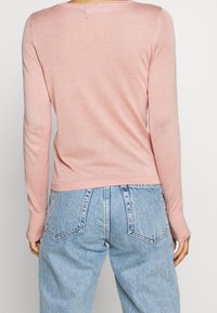 Ljusrosa långärmad tröja med en mjuk textur, rund halsringning och ribbade muddar, ihop med högmidjade ljusblå jeans.