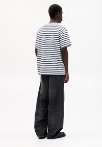 Gestreiftes T-Shirt in Weiß und Marineblau, lässiger Schnitt, kombiniert mit locker sitzenden, dunkelblauen Denim-Jeans mit Gesäßtaschen, von hinten betrachtet.